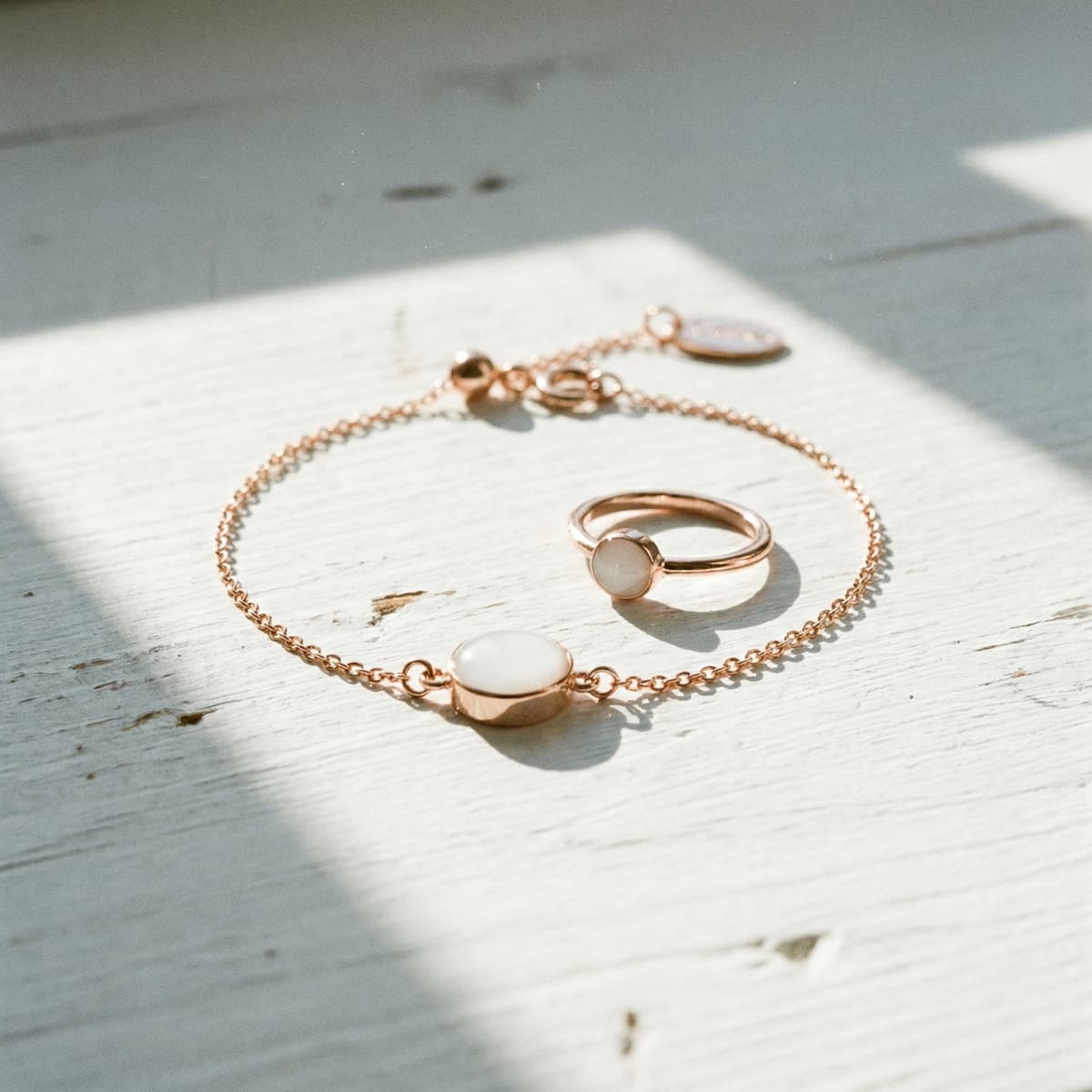 Roségoldenes Armband und Ring mit milchig-weißem Einsatz auf hellem Holzhintergrund – elegantes DIY Muttermilch Armband als persönliches Schmuckstück.