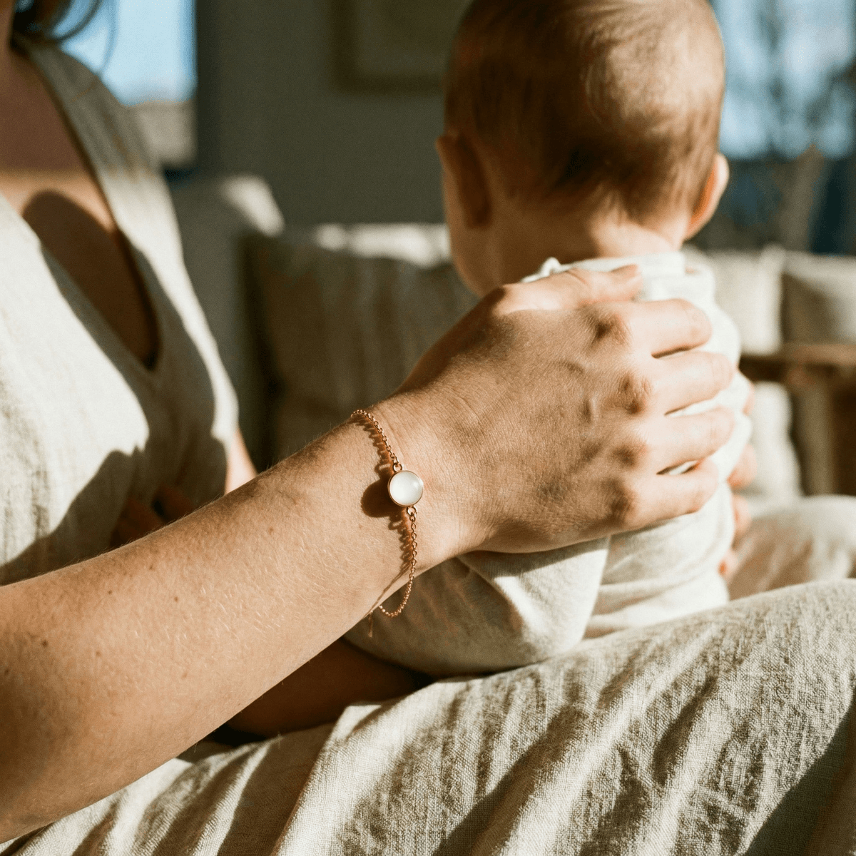 Mutter hält ihr Baby im warmen Sonnenlicht und trägt ein zartes DIY Muttermilch Armband mit milchig-weißem Stein – eine persönliche Erinnerung und ein guter Grund für ein DIY by MILKIES Kit.