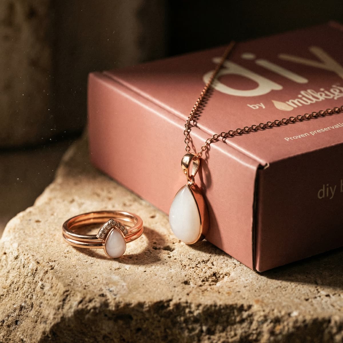 Elegantes Schmuckset als persönliches Geschenk zur Stillreise: rosegoldene Halskette und Ring mit milchig-weißem Tropfenstein in rosa DIY by MILKIES Verpackung.