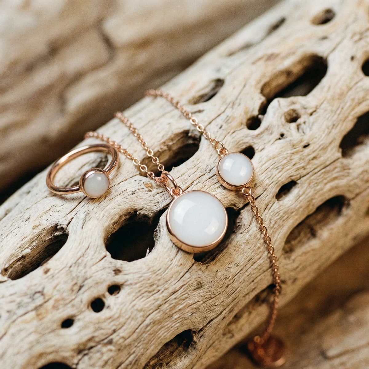 Roségoldener Schmuck mit milchig-weißen Cabochons (Ring, Kette und Armband) auf Treibholz als Erinnerungsstück, wenn die Milch versiegt.