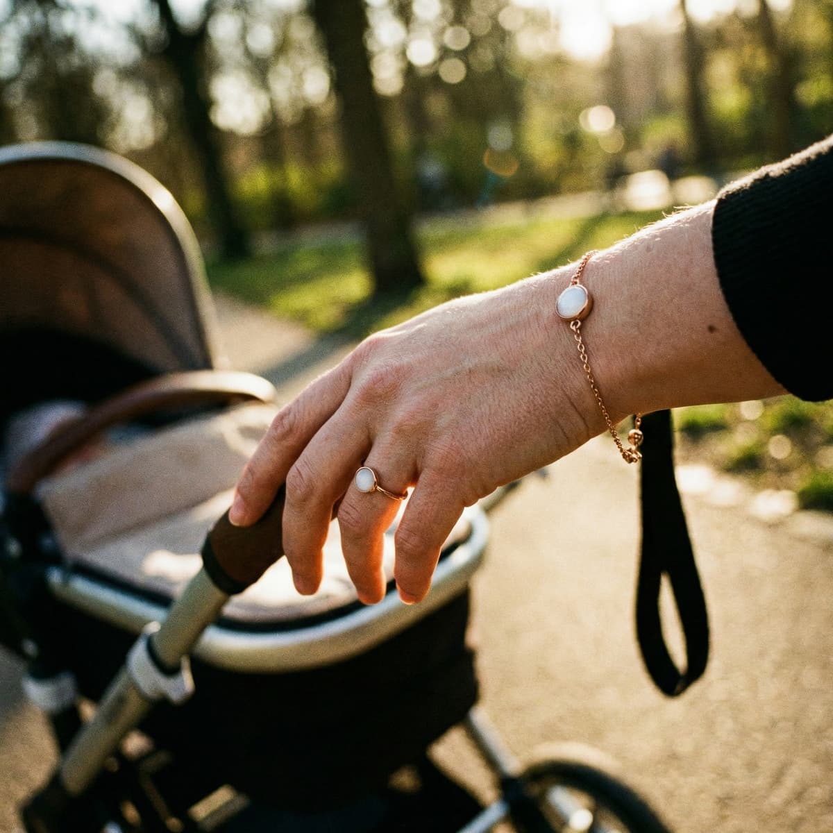 Hand einer Mutter am Kinderwagen im Park mit zartem Armband und Ring als Muttermilch Andenken in roségoldener Fassung
