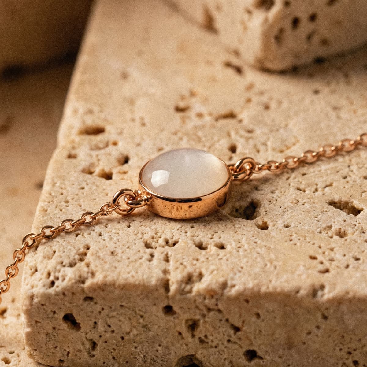 Elegantes Armband aus rosévergoldeter Kette mit ovalem, milchig-weißem Cabochon als Muttermilch Armband, in Nahaufnahme auf hellem Naturstein fotografiert.