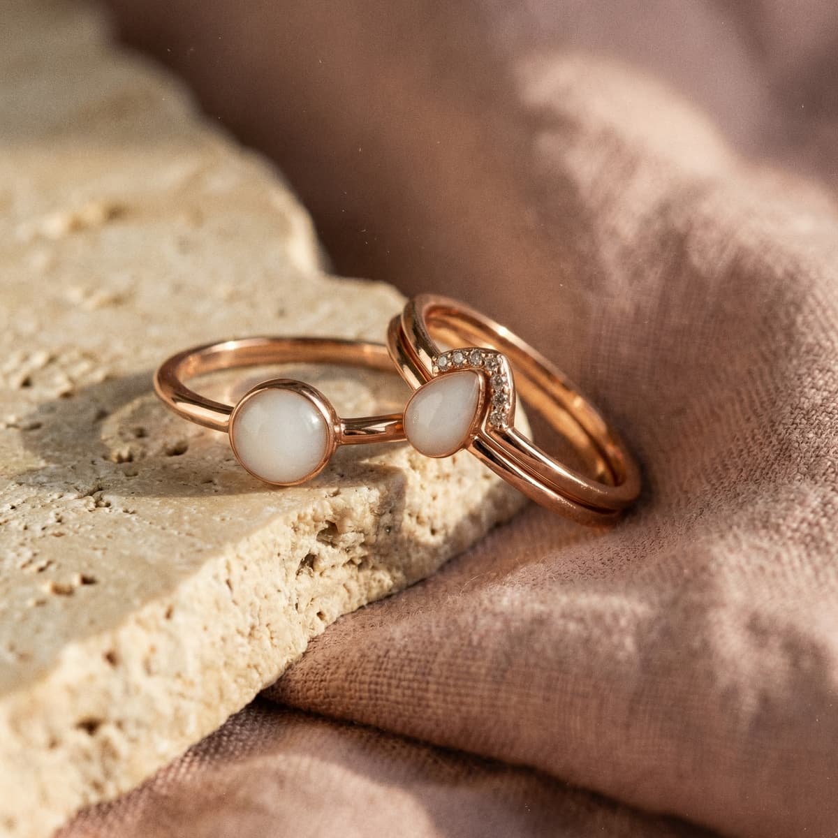 Nahaufnahme eleganter roségoldener Ringe mit milchig-weißem Stein als Muttermilch Ring auf hellem Naturstein vor weichem Stoffhintergrund.