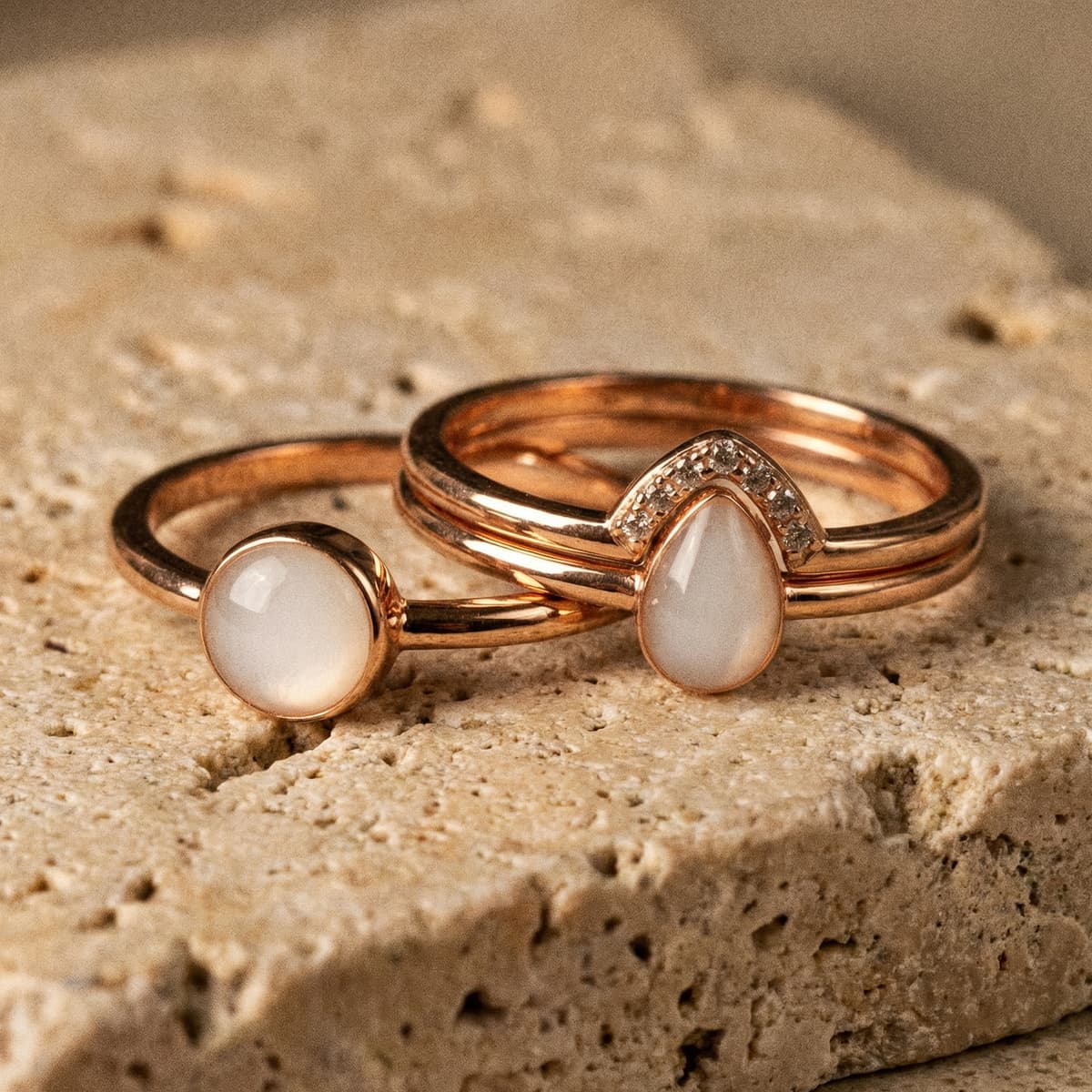 Elegantes Schmuck-Set mit drei goldfarbenen Ringen, darunter ein muttermilch ring gold mit milchig-weißem Cabochon, ergänzt durch tropfenförmigen Stein mit kleinen Zirkonia auf hellem Steinuntergrund.