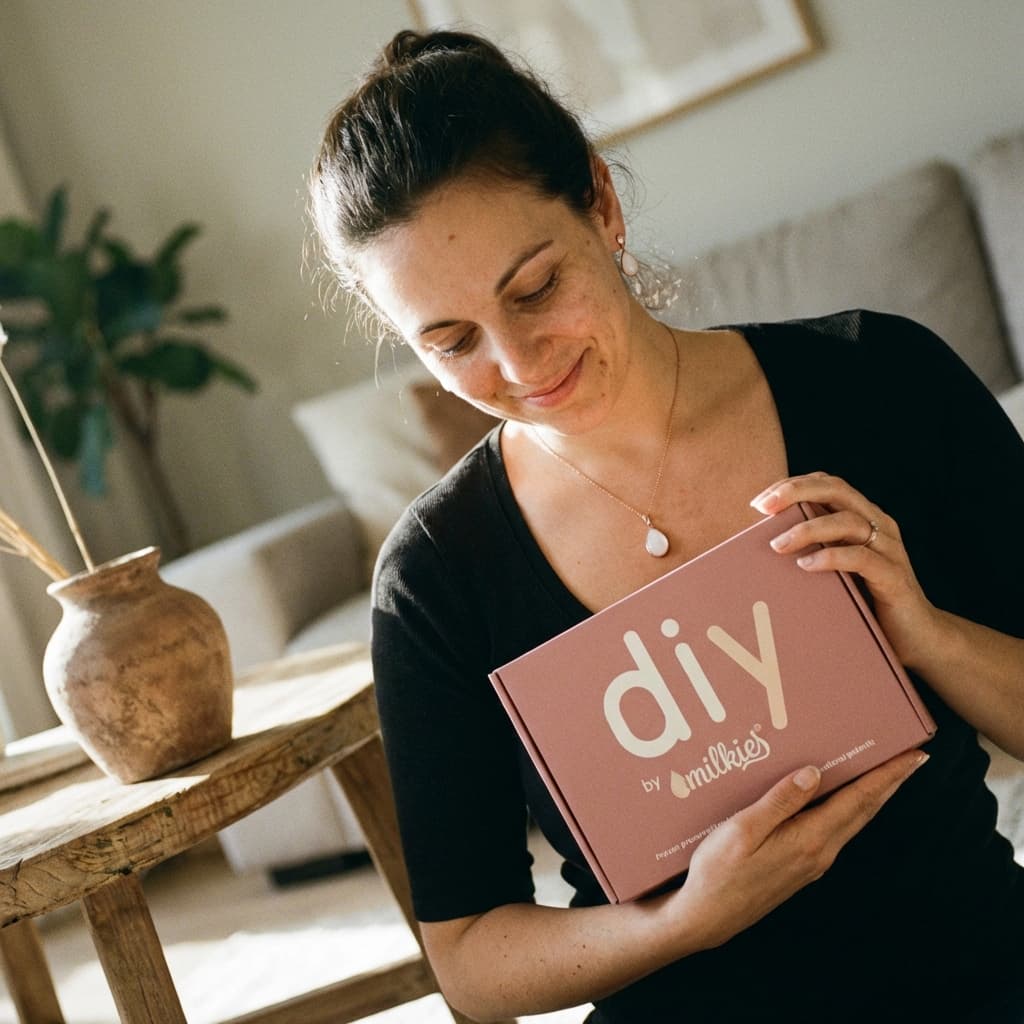 Lächelnde Frau hält eine rosa DIY by MILKIES Box in die Kamera – Muttermilch Schmuck DIY Set als gute Idee, um zuhause ein persönliches Andenken selbst zu gestalten.