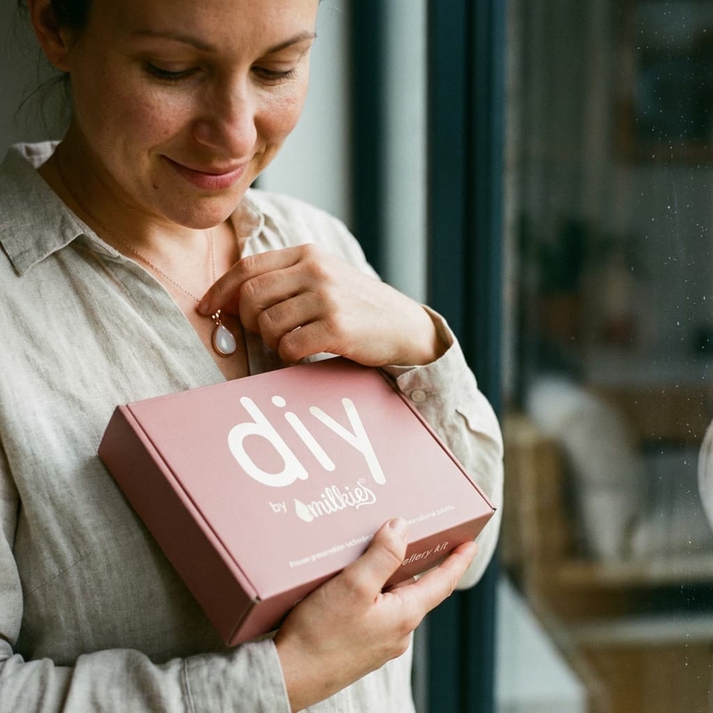Frau hält das DIY by MILKIES Set in den Händen und berührt eine milchig-weiße Kette – Muttermilchkette DIY als persönliches Erinnerungsstück, das zeigt, warum sich das DIY-Kit für Zuhause lohnt.