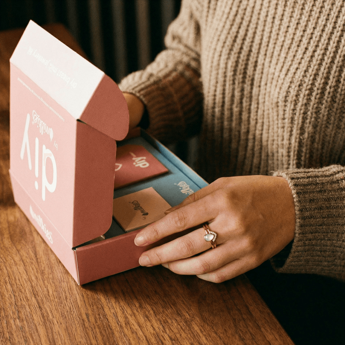 Frau öffnet das DIY by MILKIES Set am Holztisch und trägt einen Ring aus Muttermilch – ideales DIY-Kit, um ein persönliches Erinnerungsstück bequem und privat zu Hause anzufertigen.