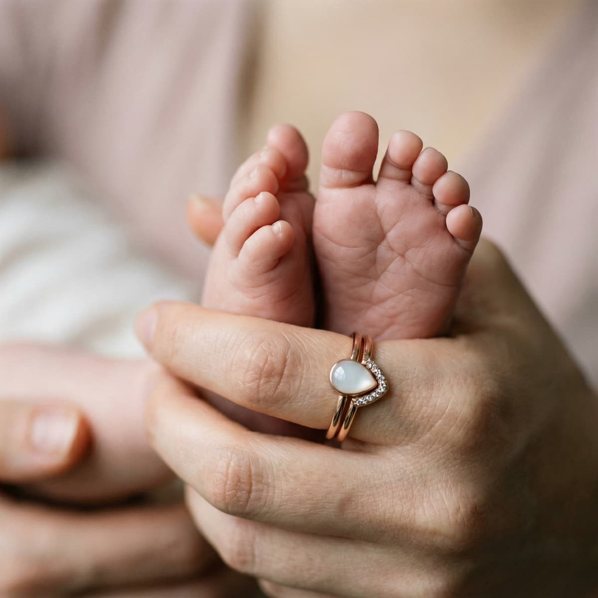 Nahaufnahme von Babyfüßen in der Hand einer Mutter mit rosegoldenem Ring und milchig-weißem Herzstein – zartes Stillandenken als Schmuck